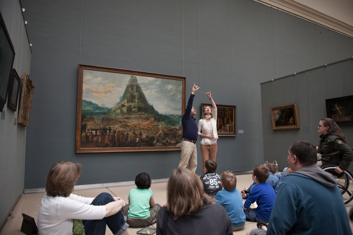 © MRBAB Two guides make a big gesture together to explain a painting to a group of people.
