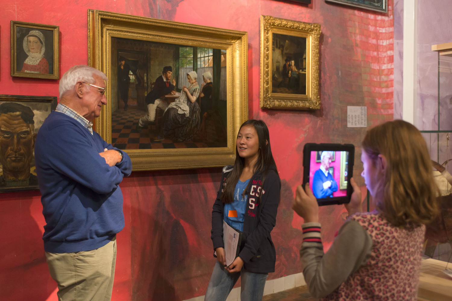 © Zeeuws Museum, Image: Anda van Riet One girl is using a tablet to film another girl who is talking with an older man, presumably about the painting behind them.