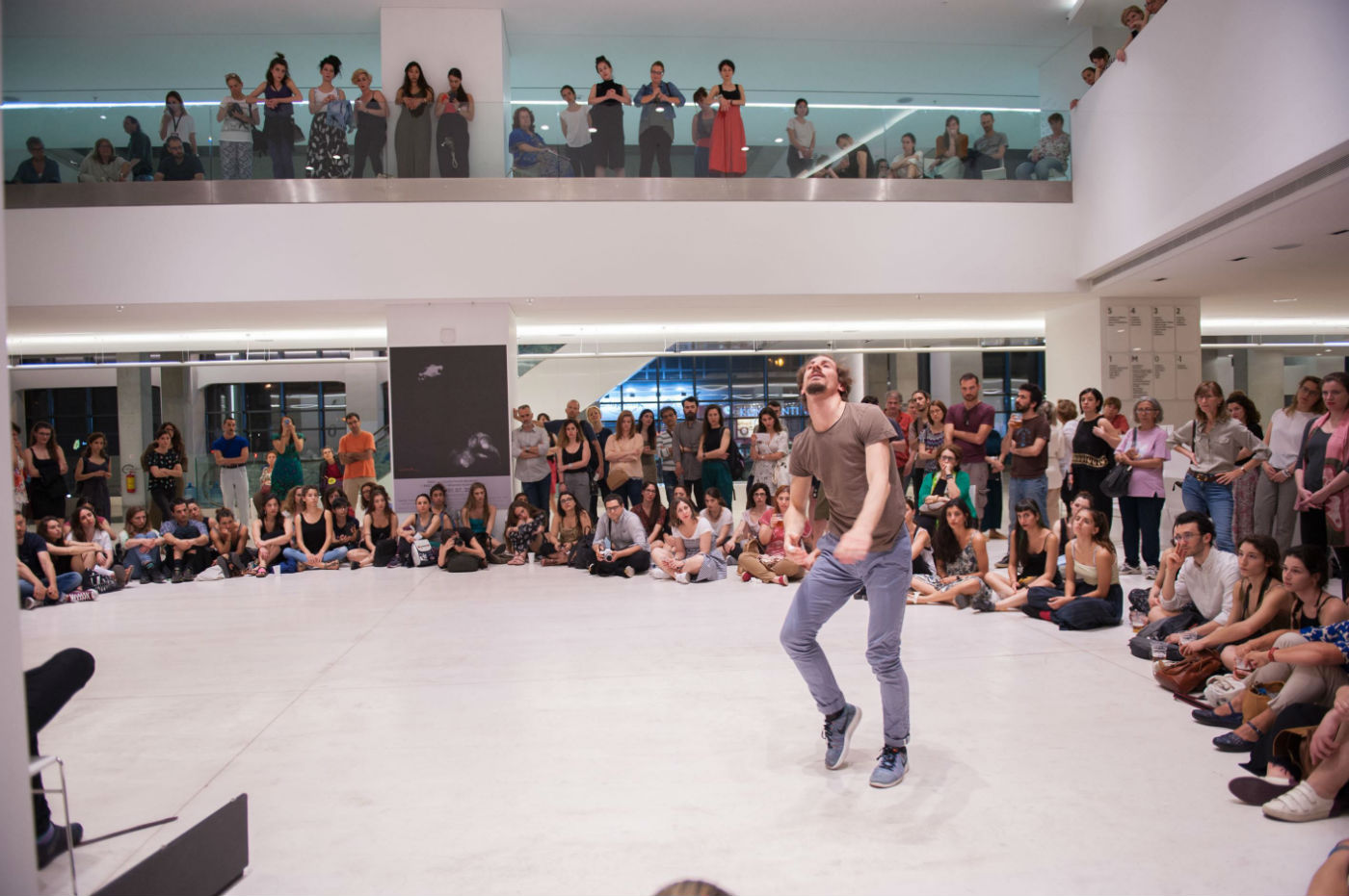  A person is dancing, surrounded by a number of people sitting or standing and watching them. 