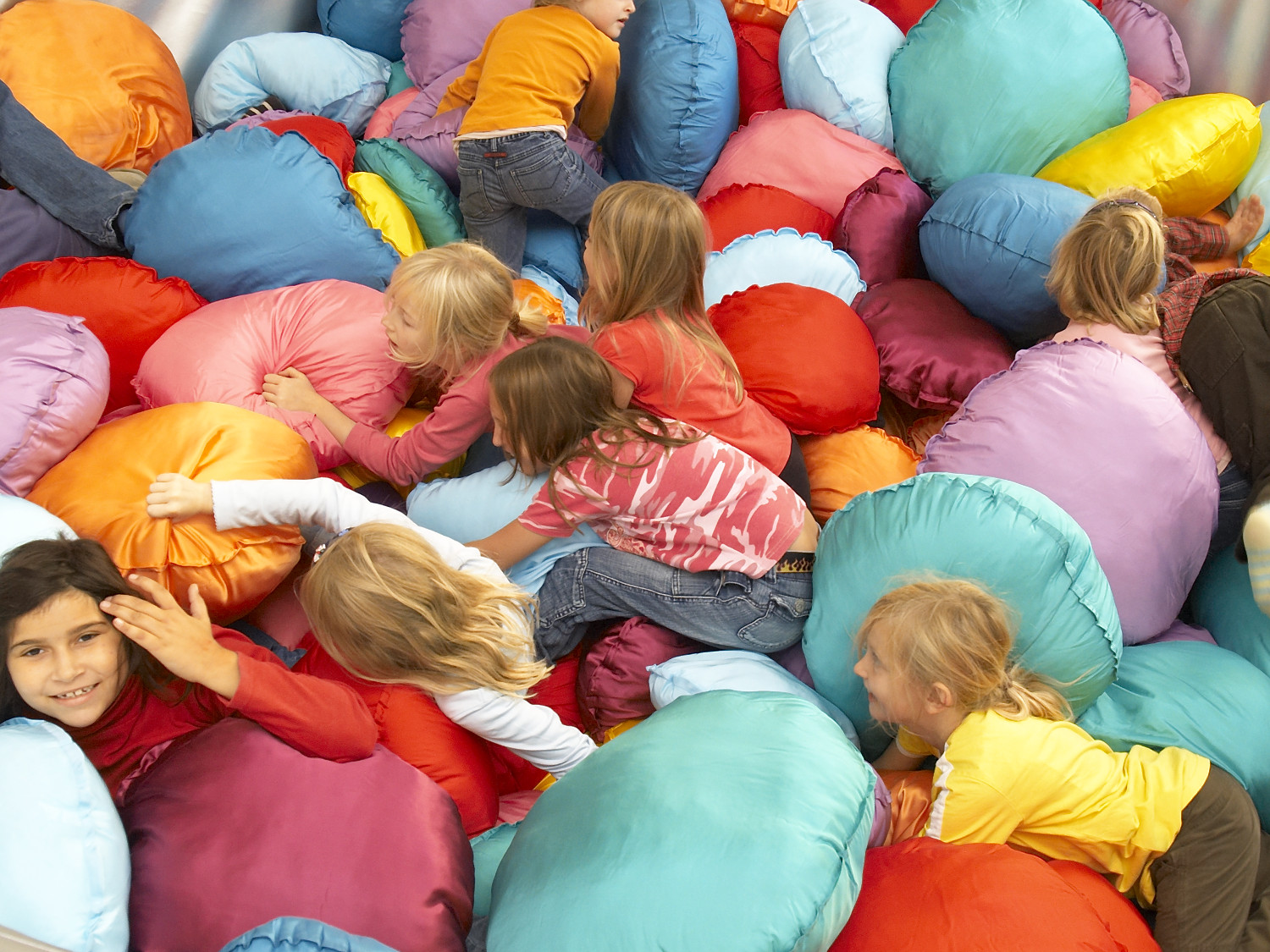  Children are crawling over numerous brightly coloured cushions. 