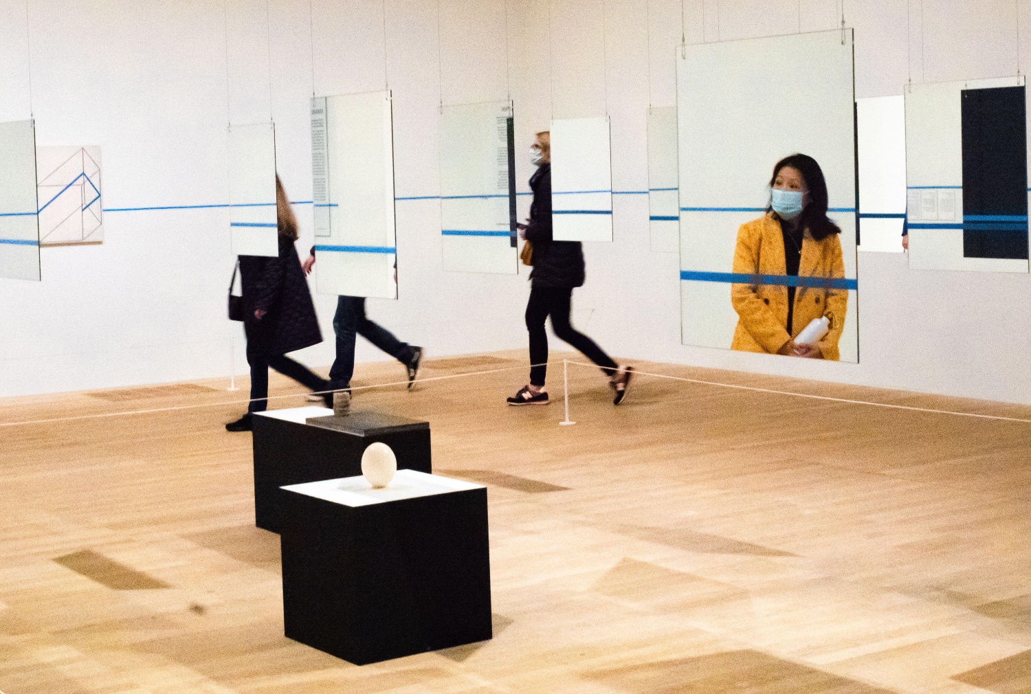  Four people walk around a contemporary art display consisting of mirrors and sockets. The face of one person is reflected by the mirror.