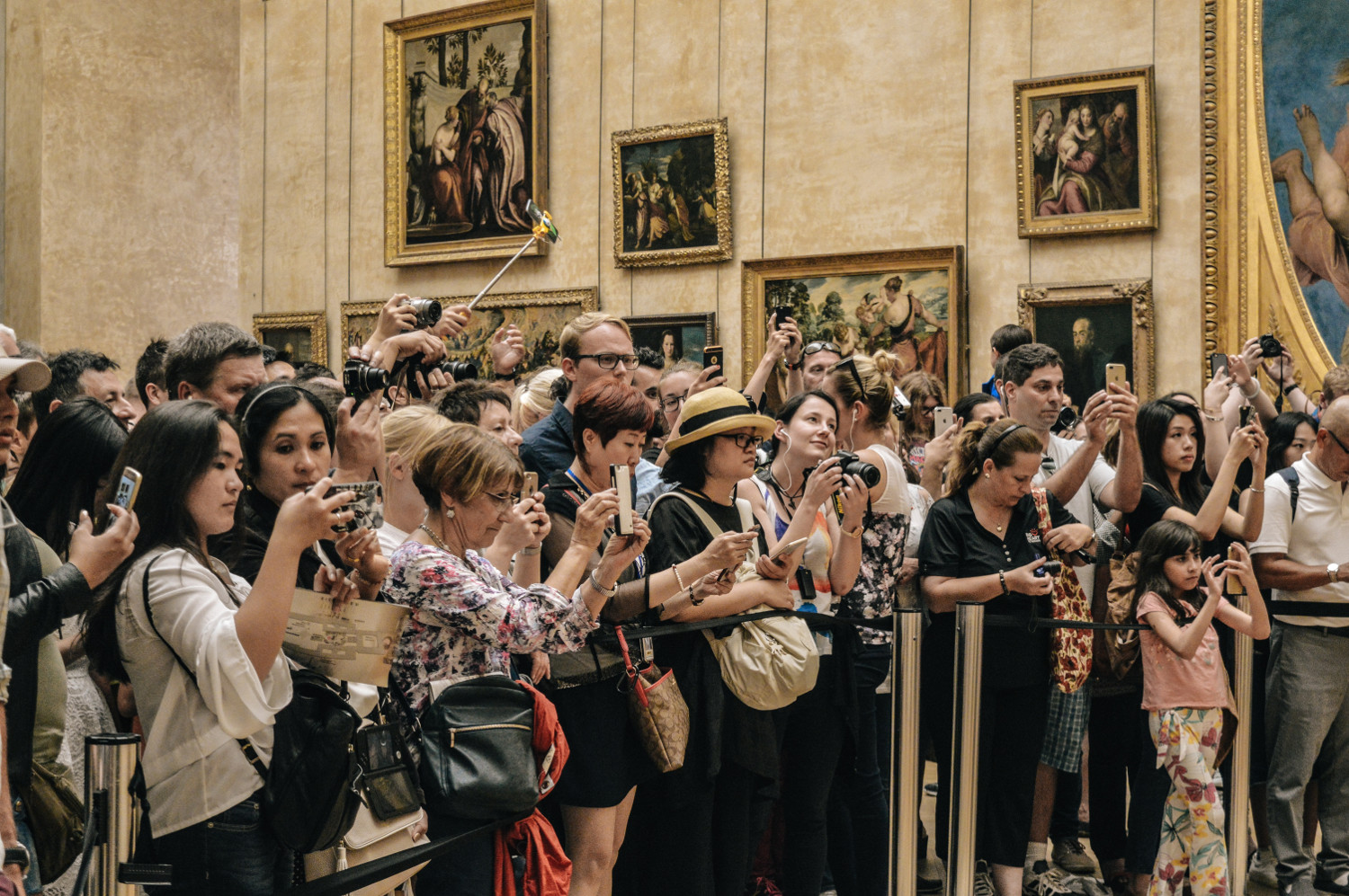 © Image: Alicia Steels A large group of tourists stand behind a rope fence inside a museum to take photos of something outside of the picture.