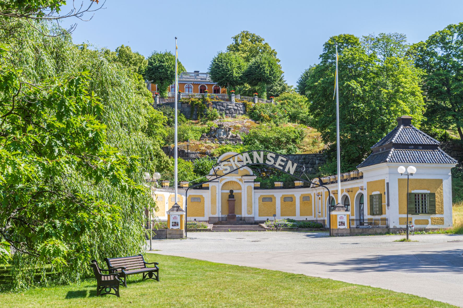 © Skansen, Image: Jonathan Lundkvist Picture of the entrance to an open-air museum. The entrance is yellow and surrounded by green trees.