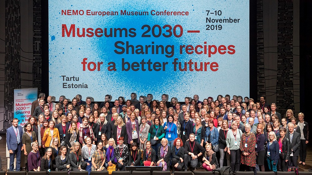 Group photo of 200 people at NEMO's European Museum Conference in 2019. They are standing in front of a projection of the conference design.   © Arp Karm