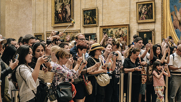 In this photo a big group of tourists stand behind a barrier rope inside a museum and take photos. The artwork which they photograph is not shown..  © Image: Alicia Steels