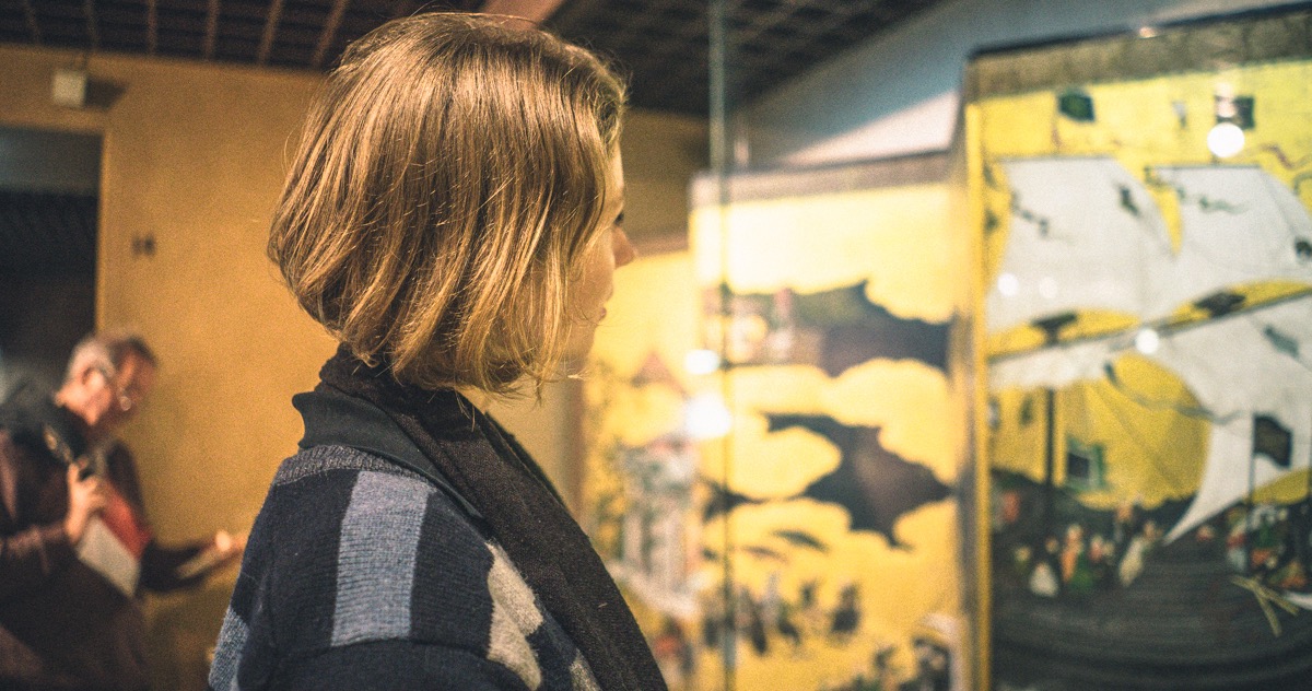  A person with shoulder length hair is looking at an art piece in a glass monter. 