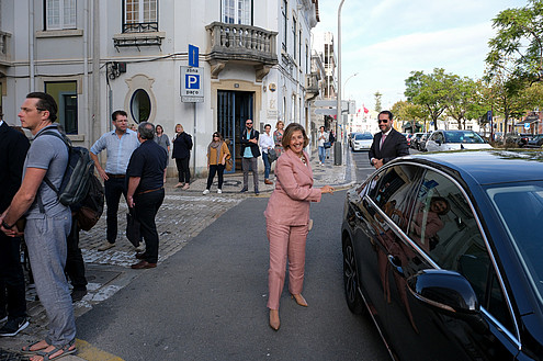 A person is standing next to a car and smiling. Around them other people are standing on the sidewalk.  © Image: Jorge Gomes