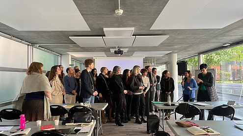 A group of people stand lined up in front of a projector screen, discussing something.  