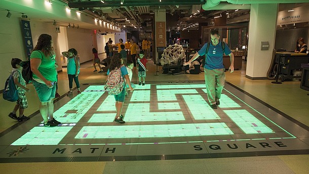  A group of children and adults interact with a digital projection on the floor.