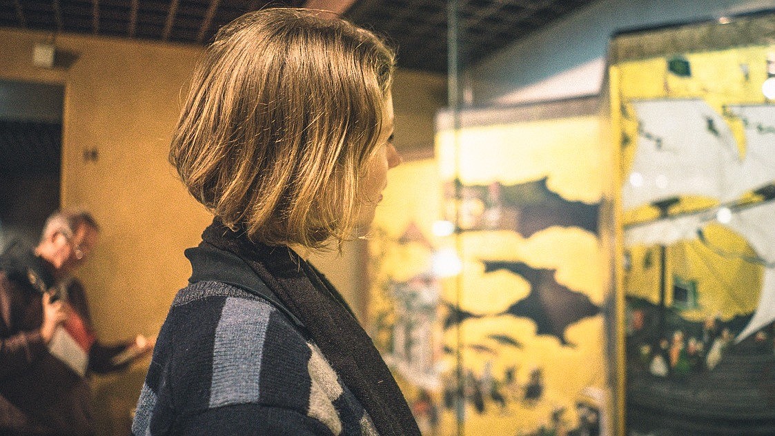© NEMO, Image: Sara Herrlander A person with shoulder length hair is looking at an art piece in a glass monter. 