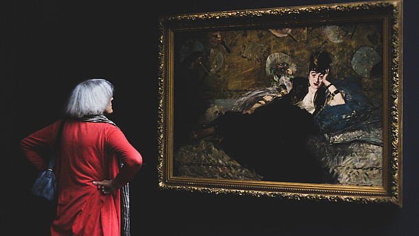  Woman with her back to the camera is looking at a painting of a person in a black dress. The wall is also black which contrasts the woman's red dress.