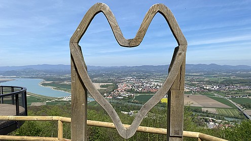 Landscape of a city is seen through a wooden heard shaped art piece.  