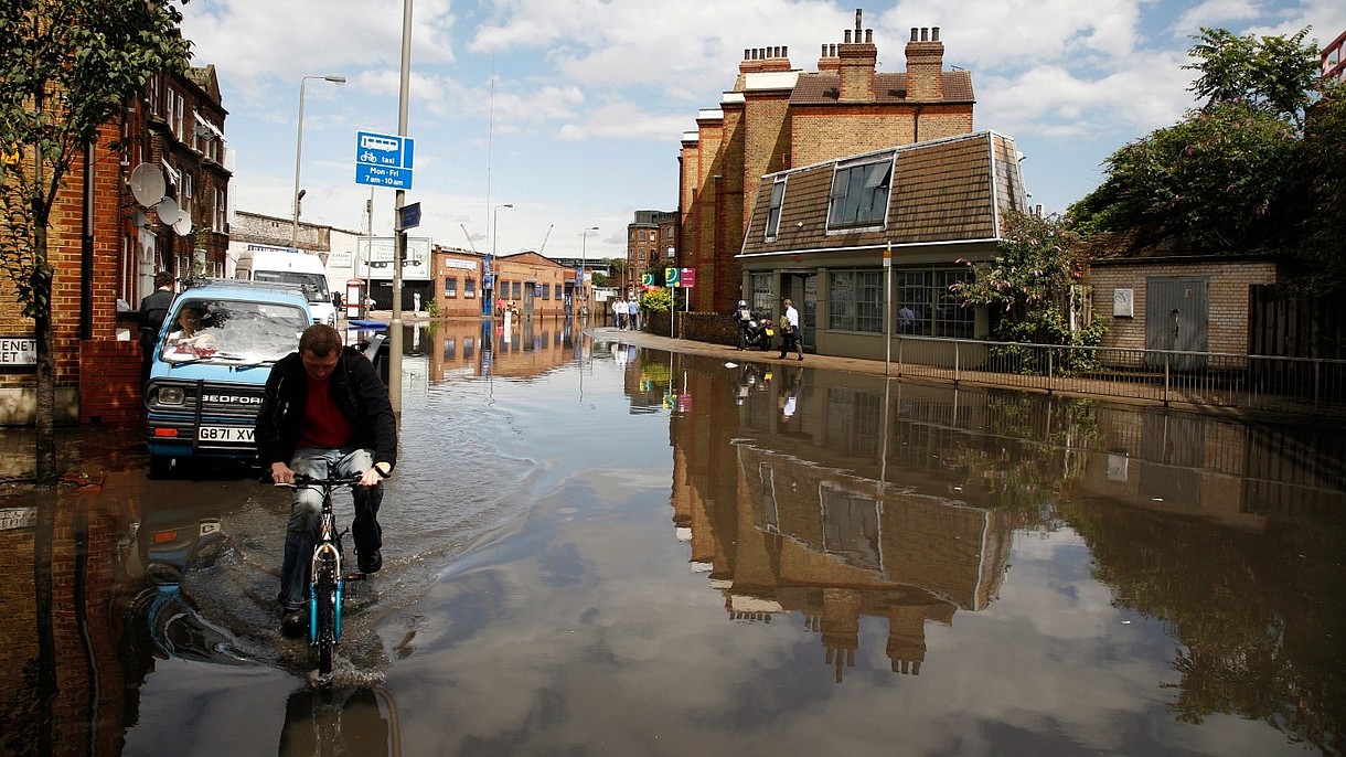 © samuel wordley / Alamy Stock Foto A person on a bicycle is riding through a flooded street in an urban setting.