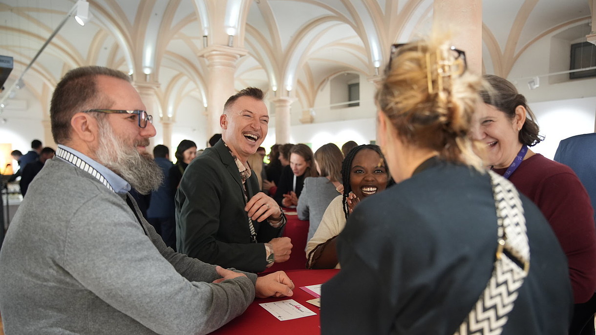 © ASTRA Museum, Image: Silviu Popa Four people stand around a table engaging in conversation and laughing. 