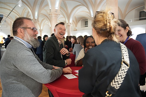 Four people stand around a table engaging in conversation and laughing.   © ASTRA Museum, Image: Silviu Popa
