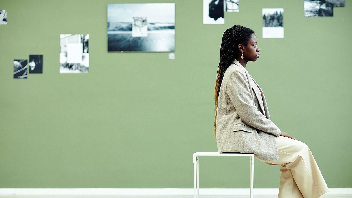 © SeventyFour Images / Alamy Stock Foto A person, photographed from the side, sits on a stool. The wall behind them is covered with black and white photographs.