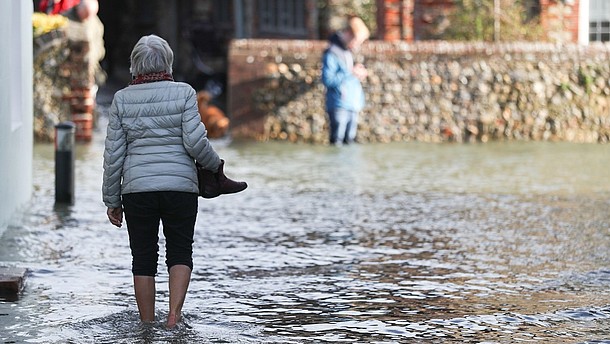  A person, photographed from the back, is walking barefoot through a flooded street. 
