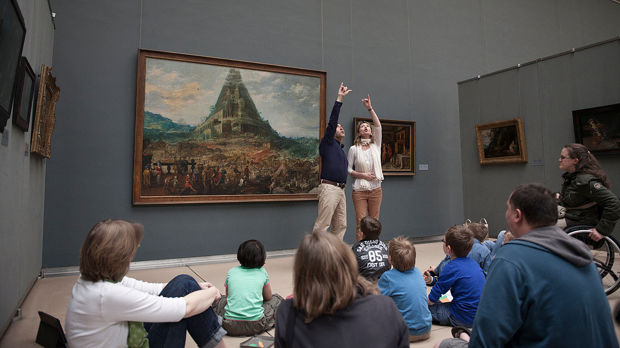 © MRBAB Two guides make a big gesture together to explain a painting to a group of people.