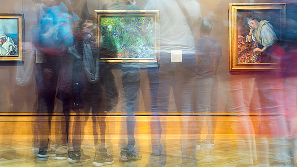  The photographer has used the slow shutter function so that it looks like several people are moving quickly in front of a wall with three pictures on it.