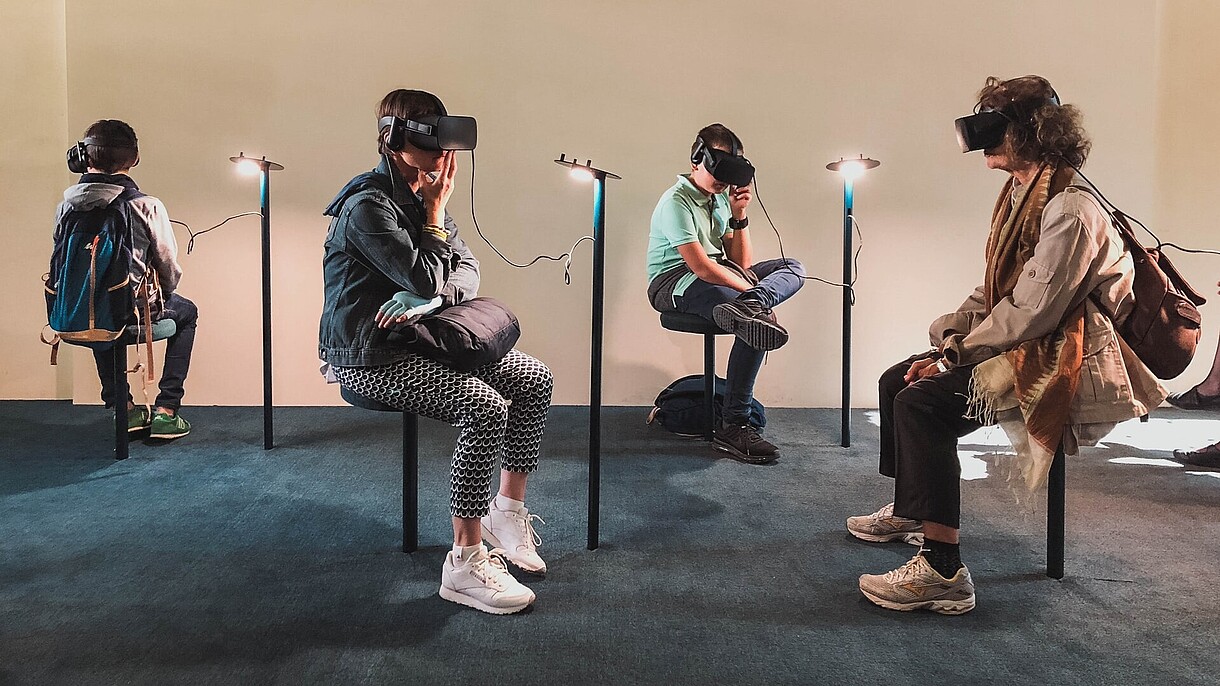© Image: Lucrezia Carnelos Four people are sitting in a gallery space. All four are wearing goggles and headphones and they are experiencing some kind of virtual reality art.