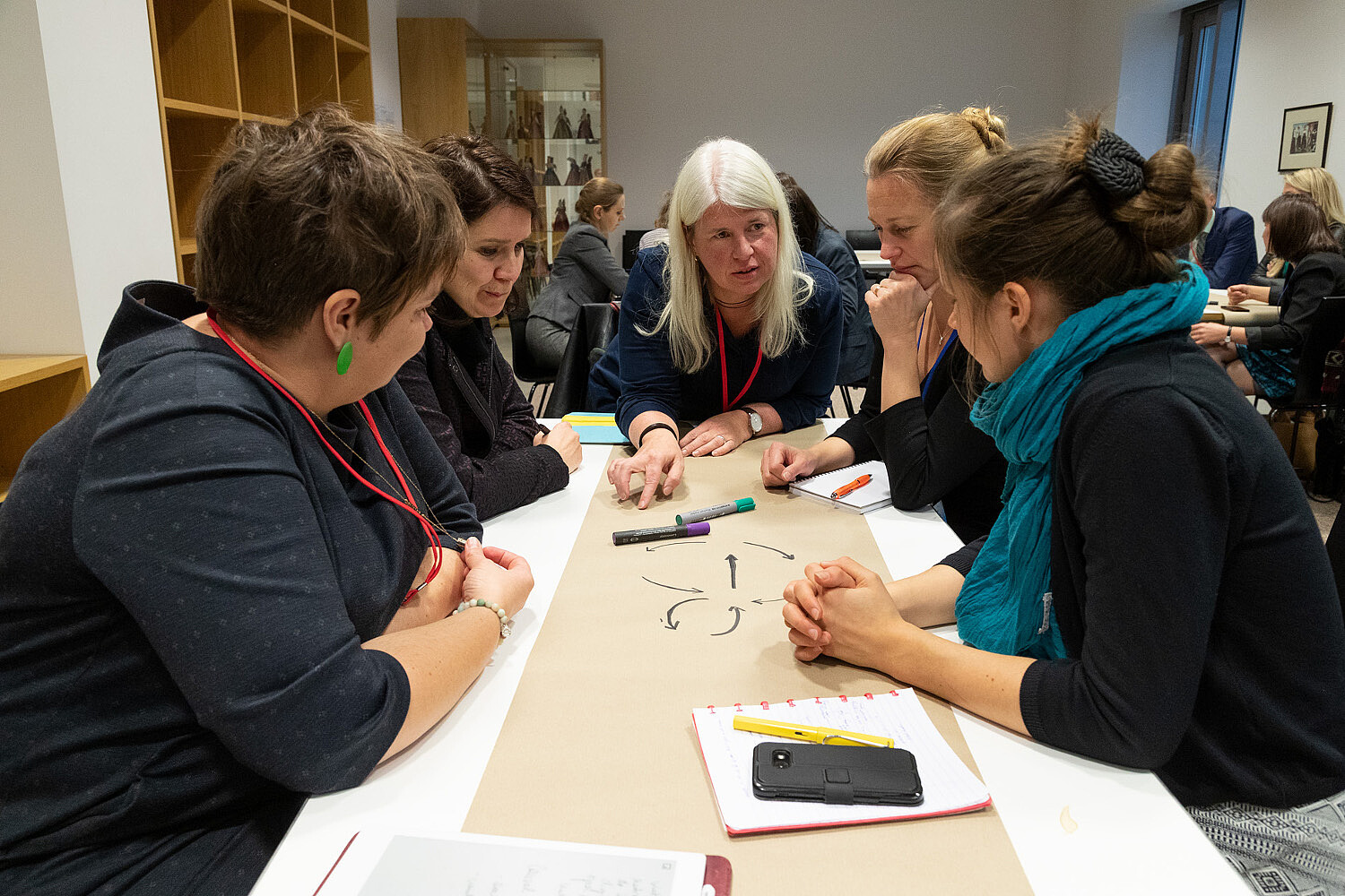 Someone leaning over a table is explaining something to a group of people sitting around it.   © Image: Berta Jänes