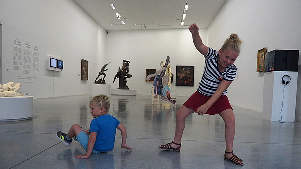  Two children are depicted dancing joyfully inside an exhibition space.