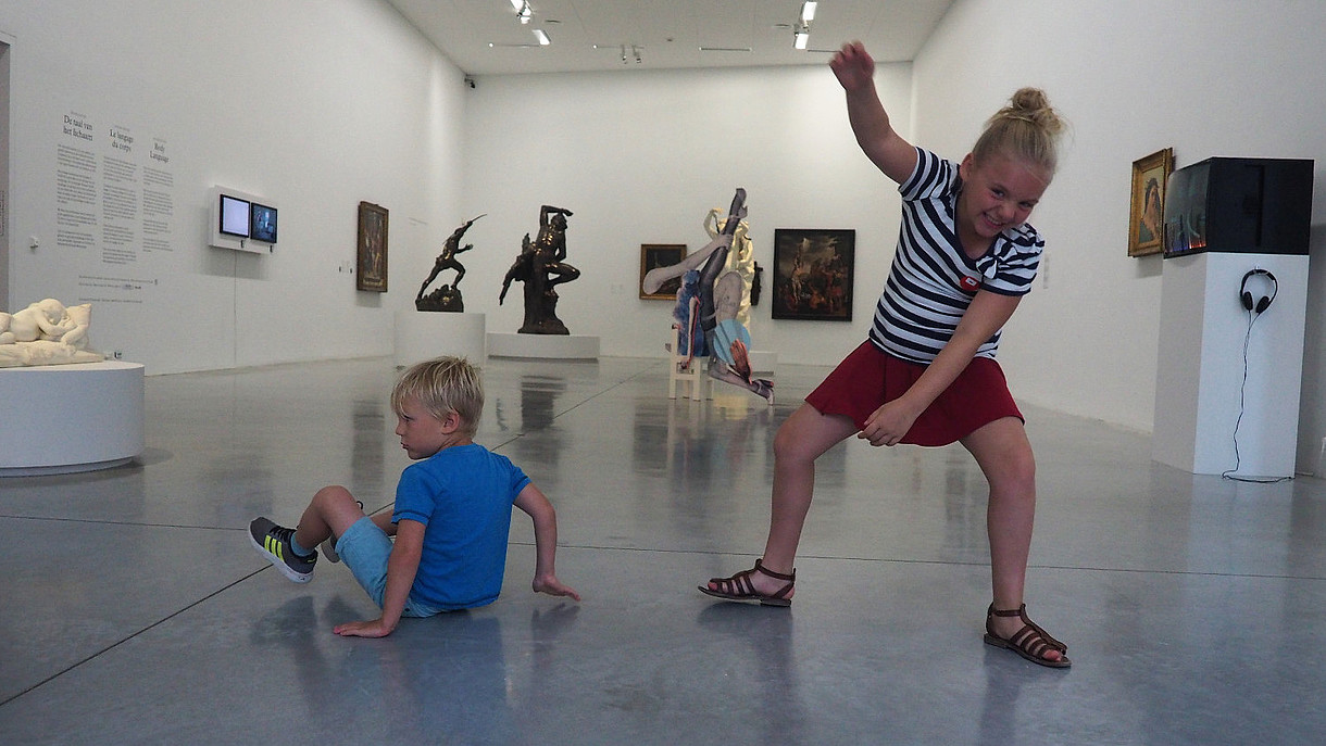 Two children are depicted dancing joyfully inside an exhibition space.