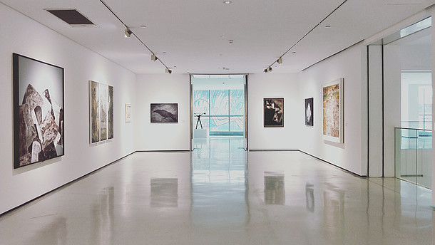  Empty gallery space with white walls, floors and ceiling. Big paintings hang on the walls.