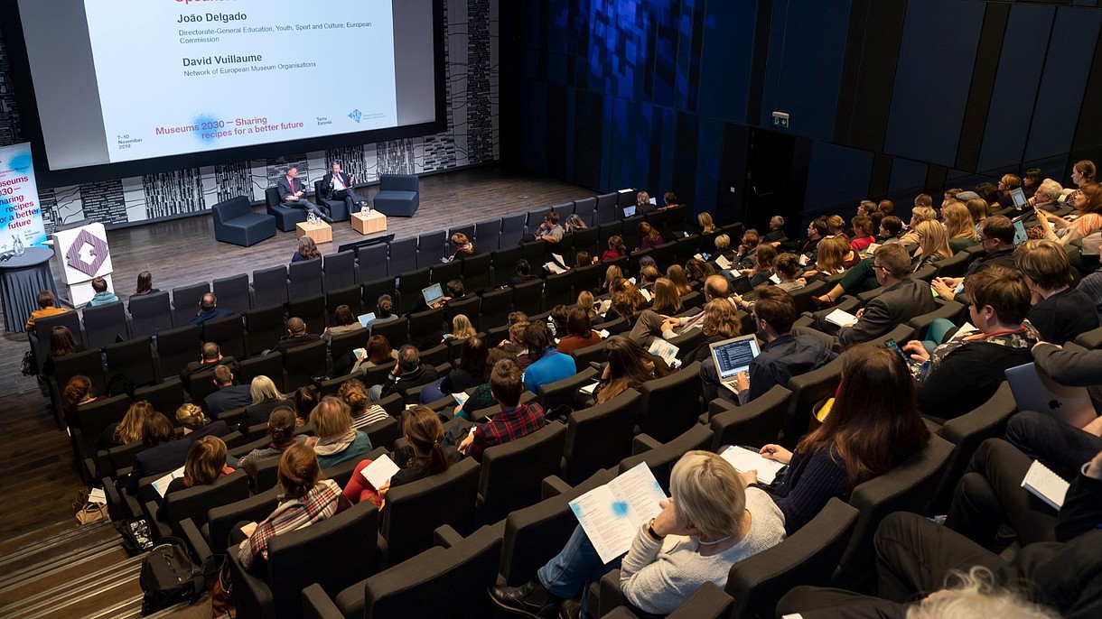 © Image: Arp Karm Auditorium full of people looking at two people on the stage. A sign shows that they are discussing EU culture policy. 