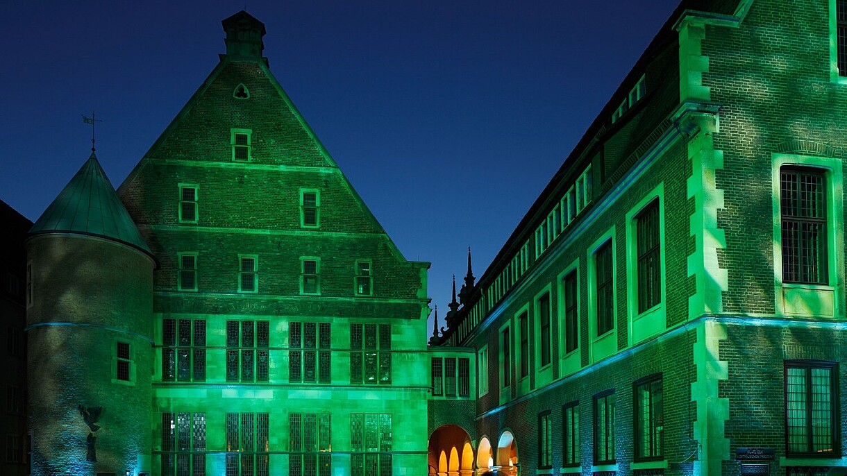 © Werner Otto / Alamy Stock Foto An old brick building is lit by green spotlights. In front of it numerous people have gathered to watch it.