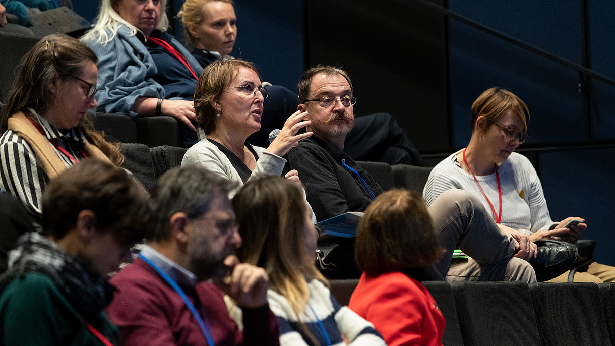 © Image: Berta Jänes A person sitting in an audience uses a microphone to ask a question. 